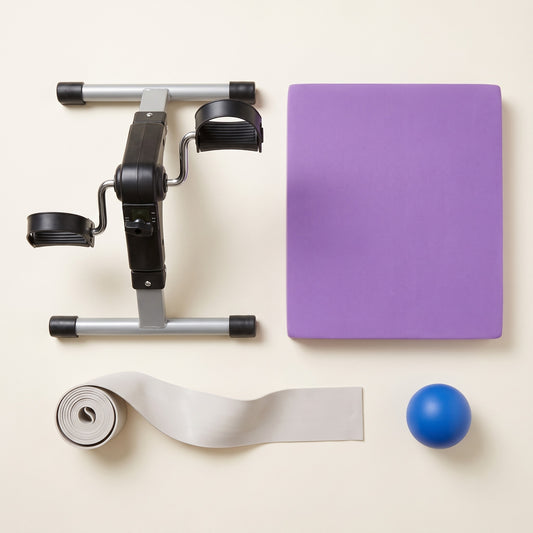 Overhead view of everything included in The Complete Basics Kit: a mini pedal exerciser, a purple balance pad, a two-metre long resistance band and a blue soft grip strength ball.