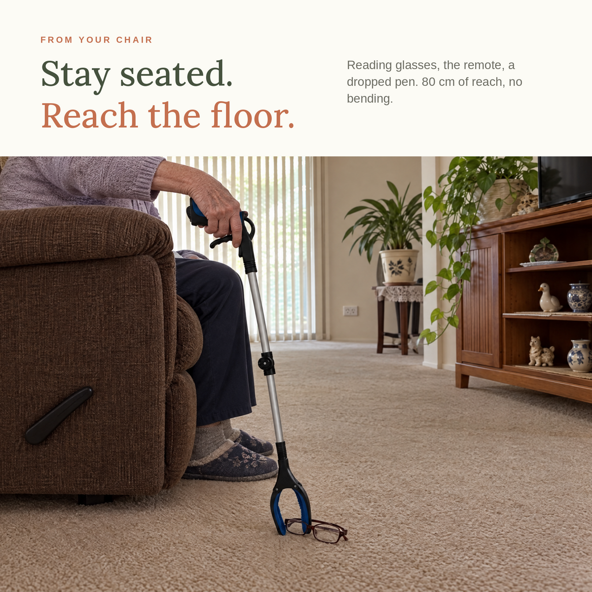 Seated in an armchair, using the foldable grabber to pick reading glasses up off the carpet