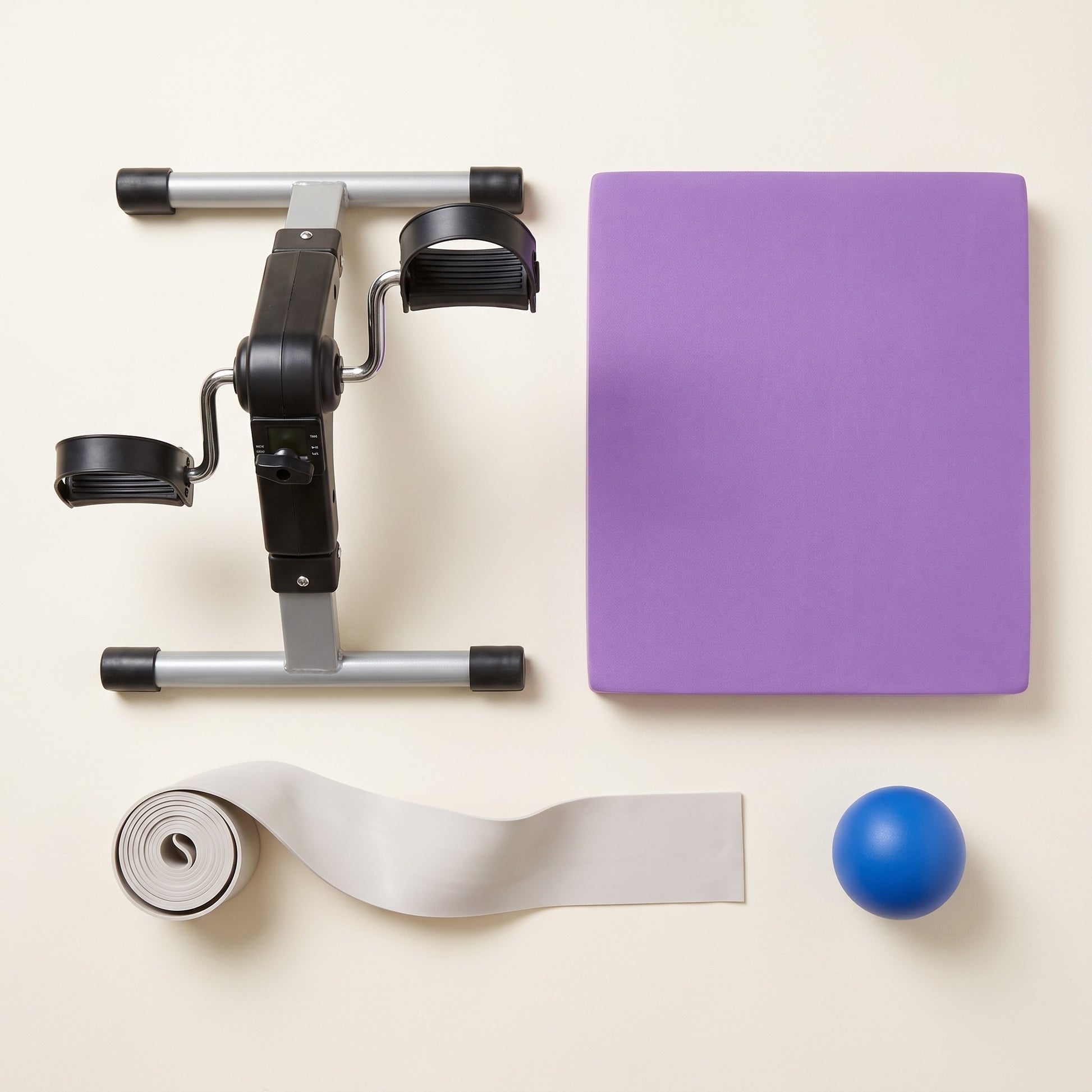 Overhead view of everything included in The Complete Basics Kit: a mini pedal exerciser, a purple balance pad, a two-metre long resistance band and a blue soft grip strength ball.