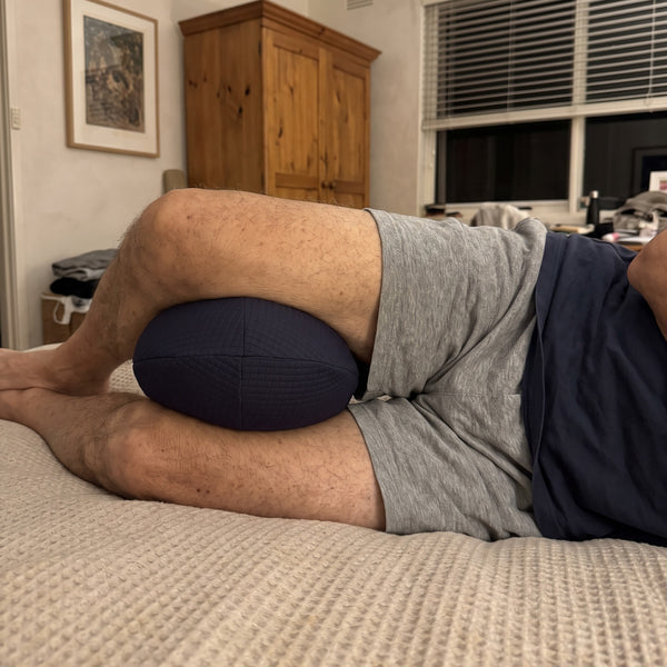 Man lying on his side with the Bean Knee Pillow between his knees