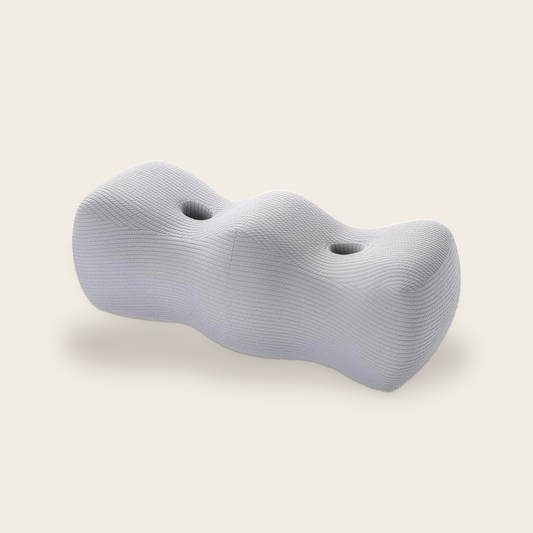The Comfort Leg Pillow in light grey, memory foam with two leg grooves, on a cream background