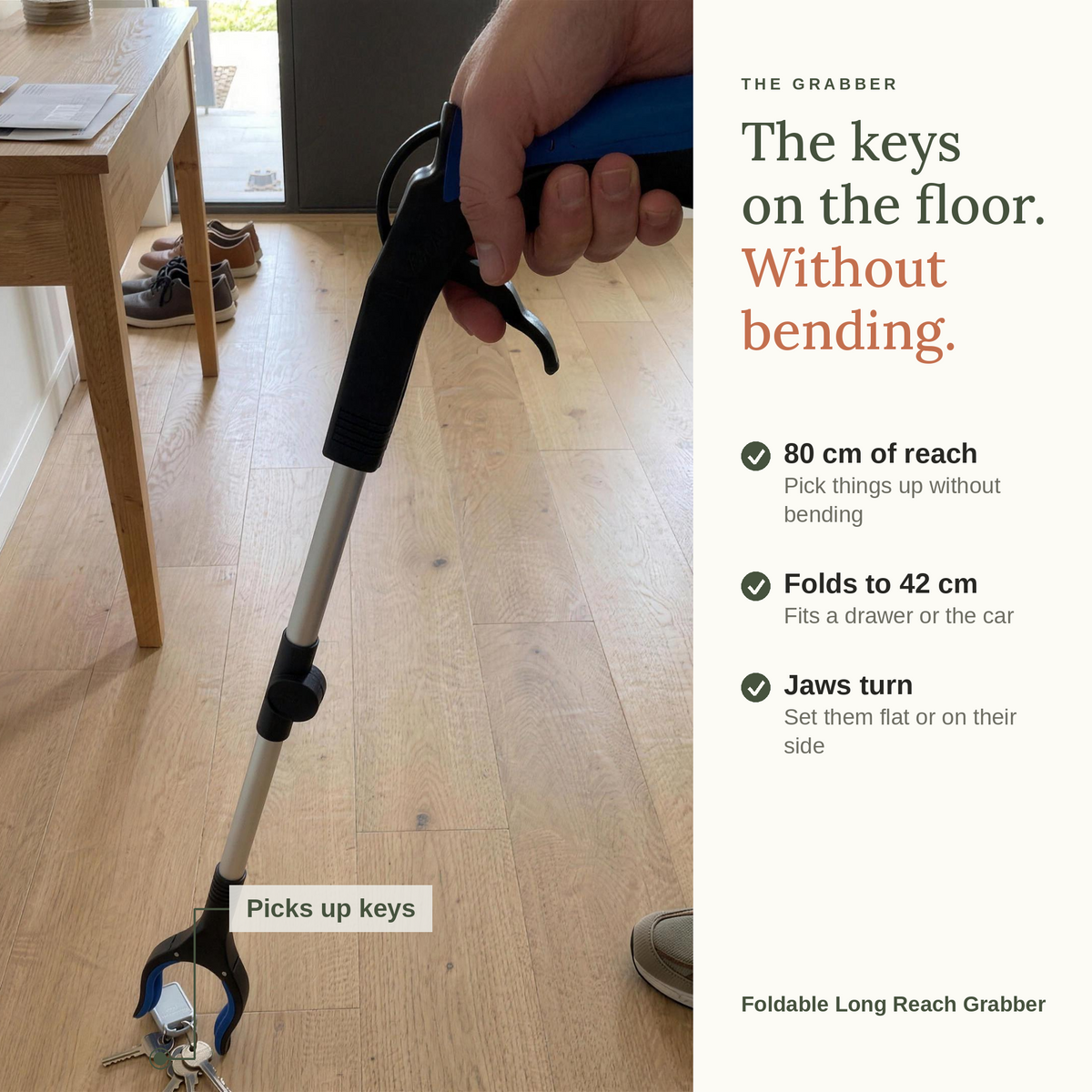 The keys on the floor, without bending. The foldable long reach grabber picking up keys from a timber floor. 80 cm of reach, folds to 42 cm, and the jaws turn flat or on their side.