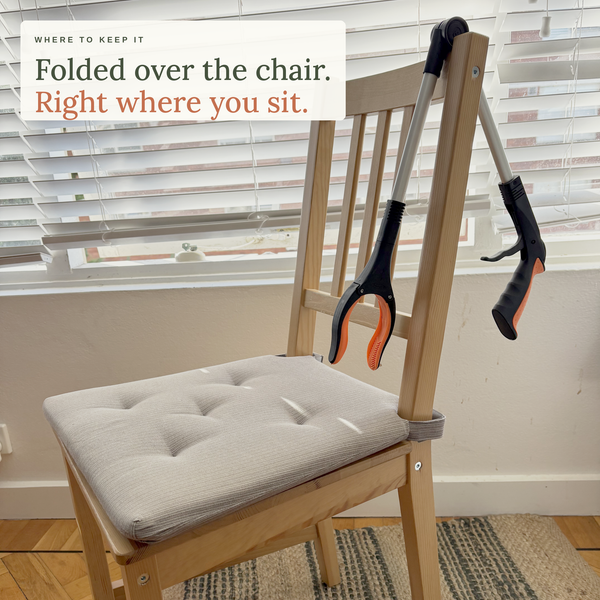 The Foldable Long Reach Grabber folded at the hinge and hanging over the back of a dining chair at home