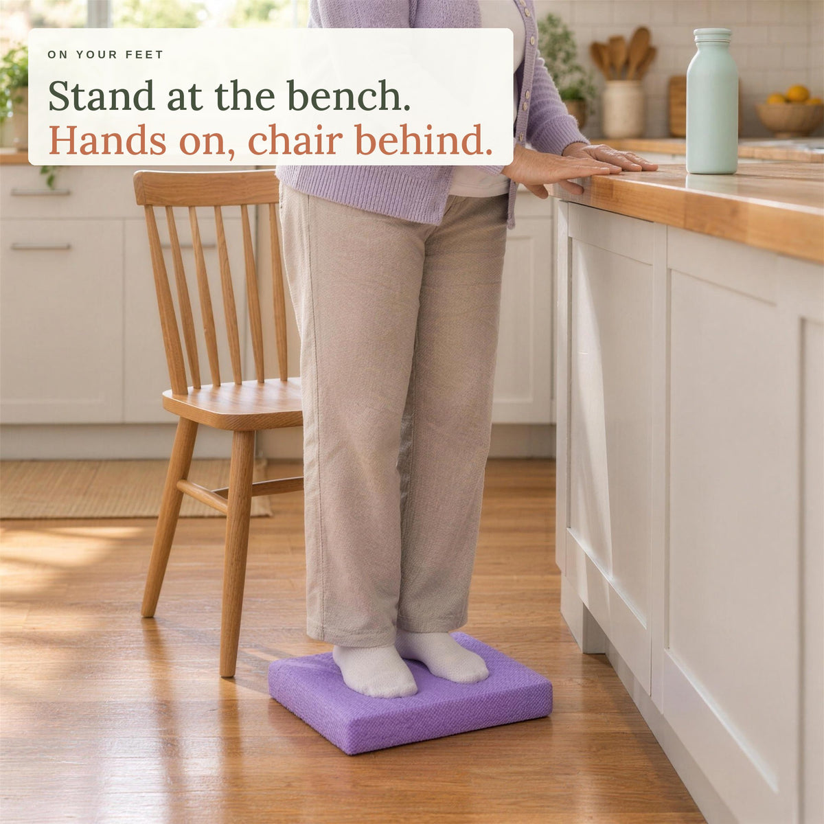 Standing on the balance pad at the kitchen bench, hands on the bench and a chair behind