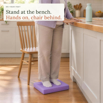 Standing on the balance pad at the kitchen bench, hands on the bench and a chair behind