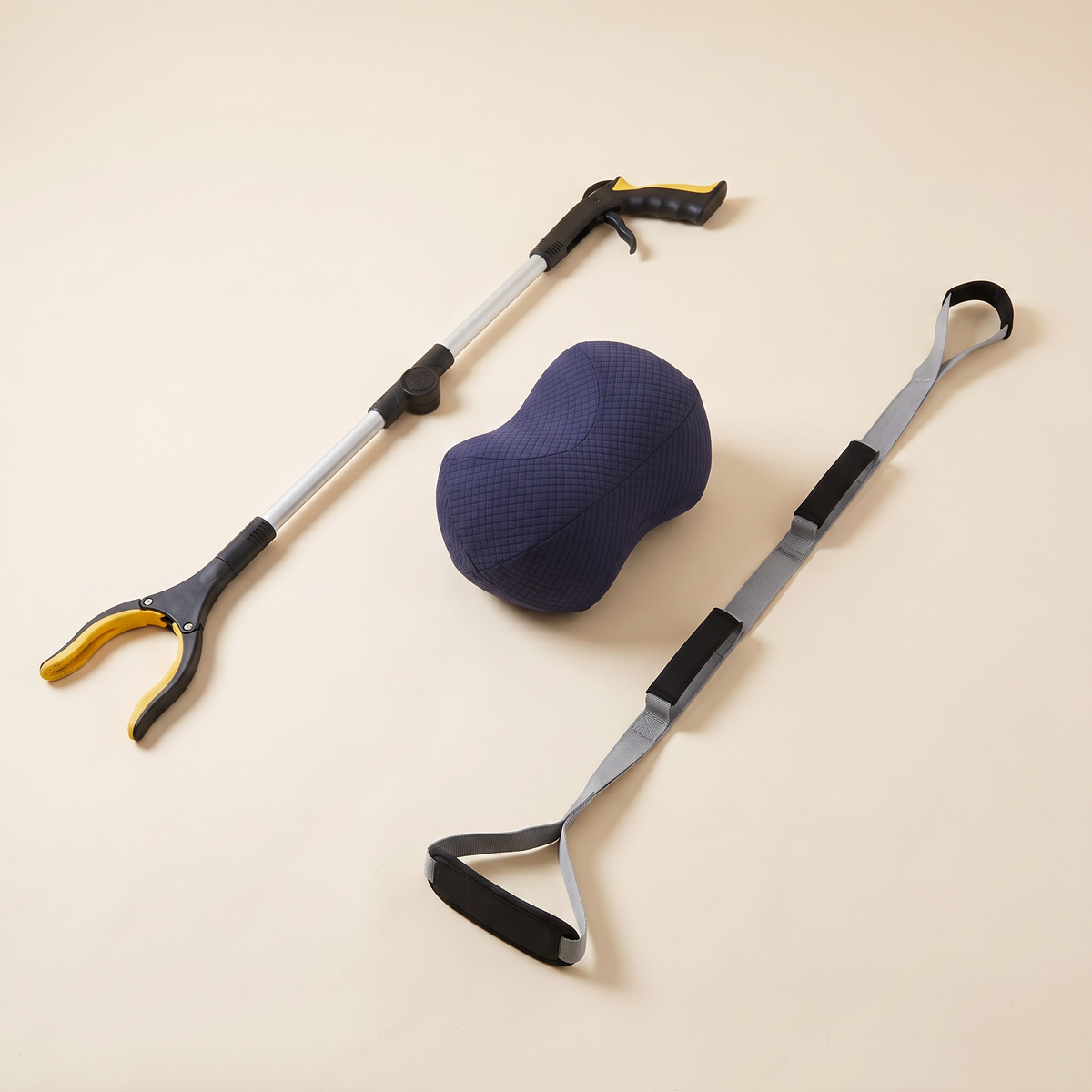 Everyday Independence & Comfort Kit on a cream background: foldable long reach grabber, navy bean knee pillow and triple grip leg lifter strap.