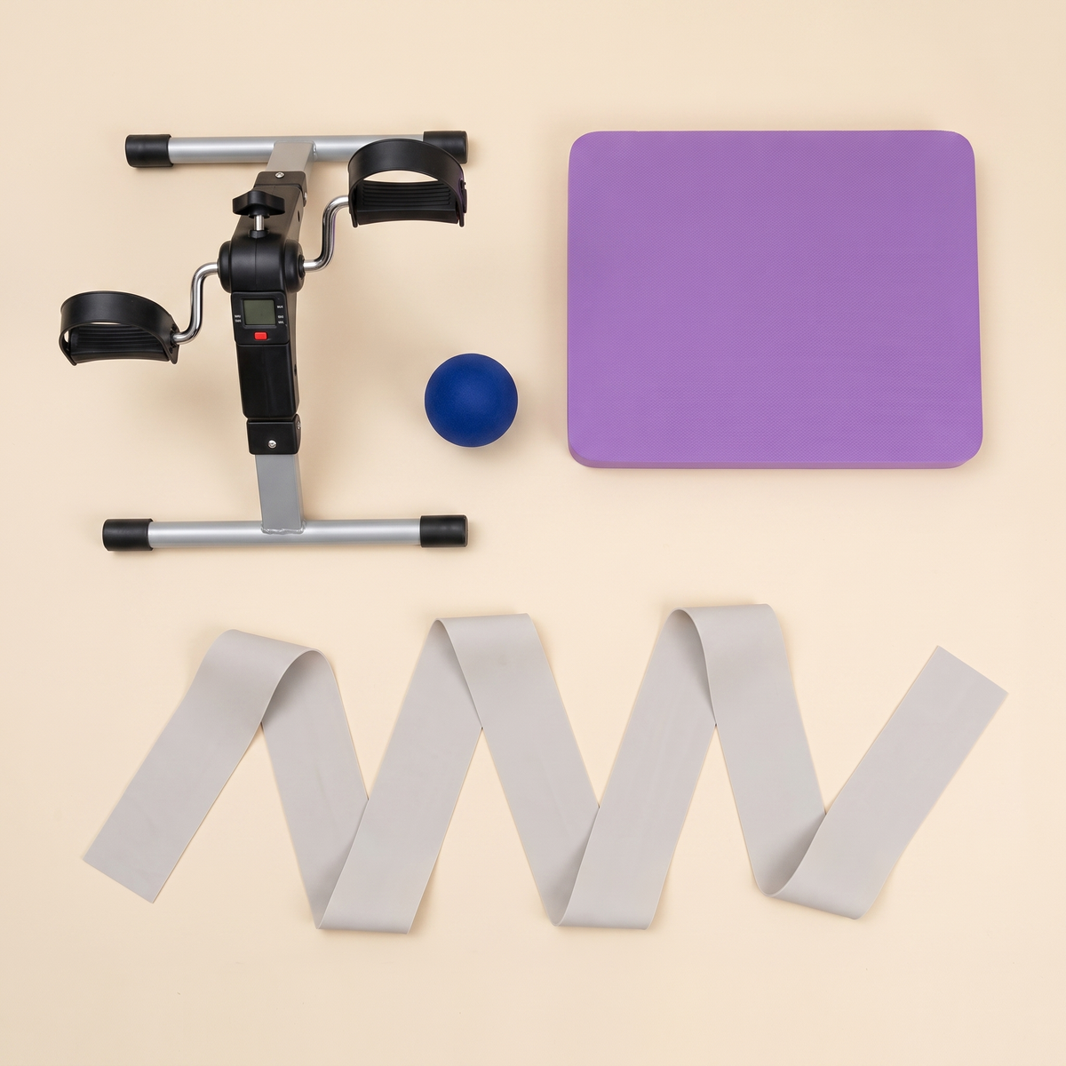 The Complete Basics Kit laid out: mini pedal exerciser, purple balance pad, soft grip strength ball and the long resistance band unrolled to show its two metre length.
