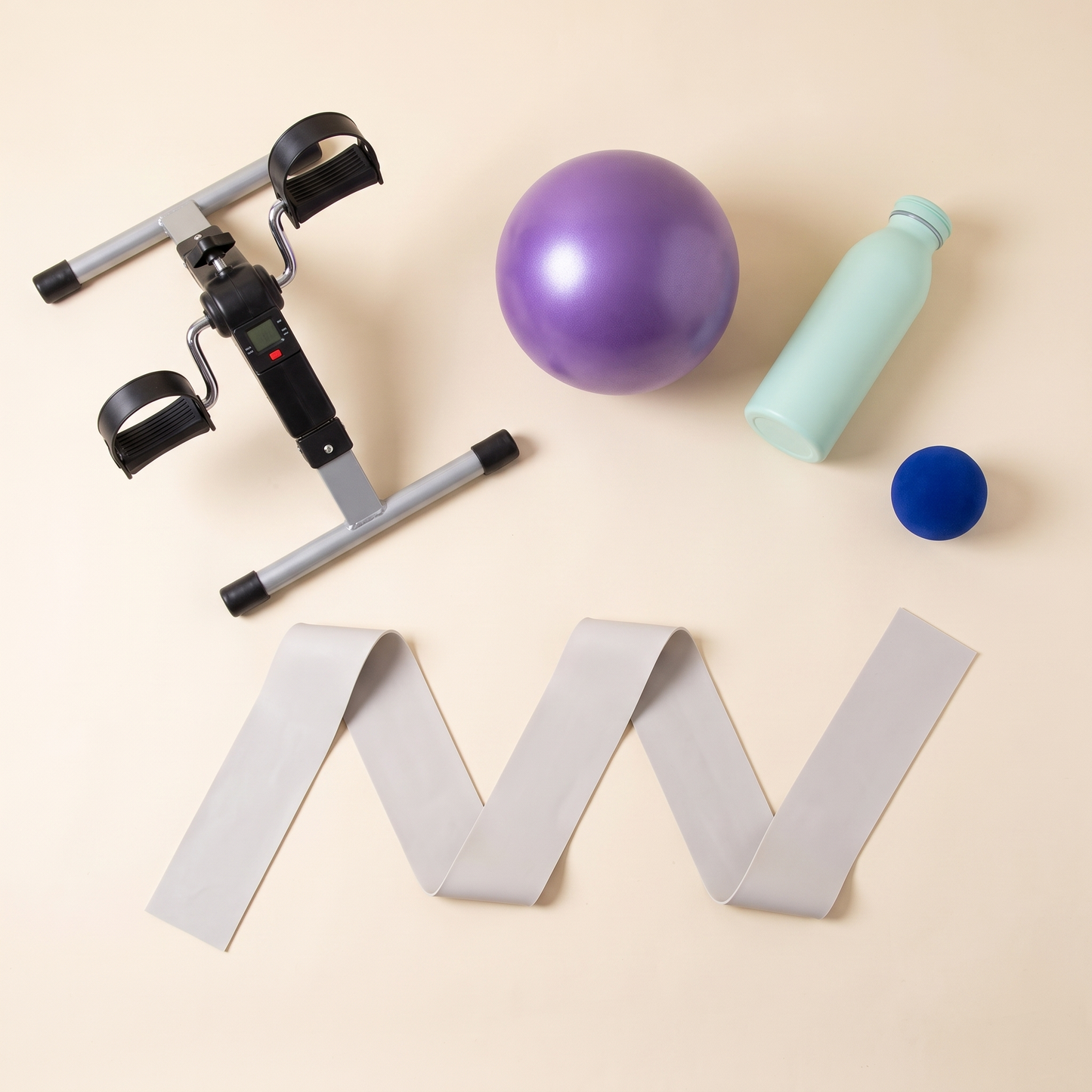 The Home Exercise Essentials Kit laid out: mini pedal exerciser, purple mini exercise ball, mint green water bottle, soft grip strength ball and the long resistance band unrolled to show its two metre length.