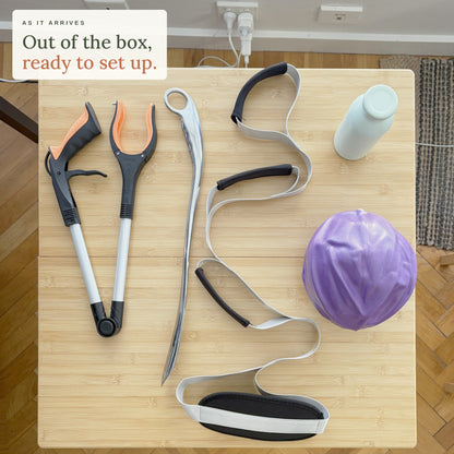 As it arrives. Out of the box, ready to set up: the Hip Replacement Ready Kit on a kitchen table seen from above, with the grabber, leg lifter, steel shoe horn, mini exercise ball and bottle