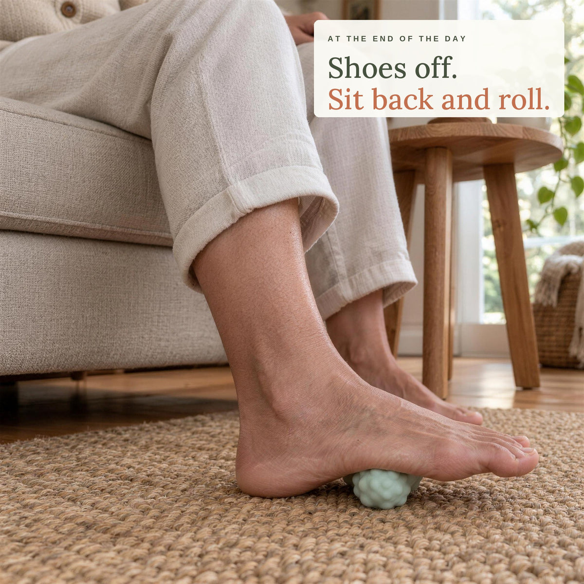 A woman in an armchair resting her bare foot on the Peanut Massage Ball