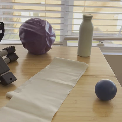 The Home Exercise Essentials Kit on a kitchen table at home: mini pedals, long resistance band, mini exercise ball, soft grip ball and bottle