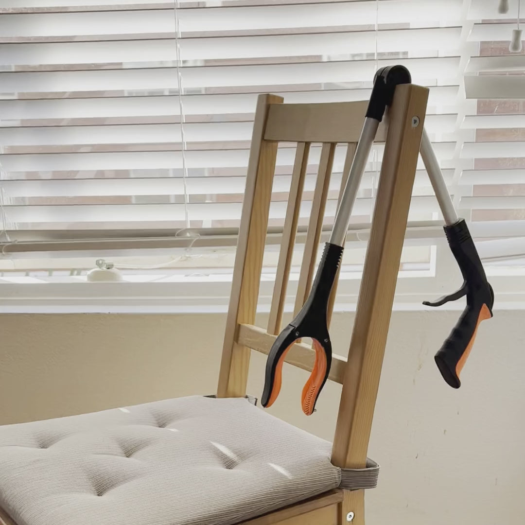 The Foldable Long Reach Grabber folded at the hinge and hanging over the back of a dining chair at home