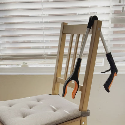 The Foldable Long Reach Grabber folded at the hinge and hanging over the back of a dining chair at home