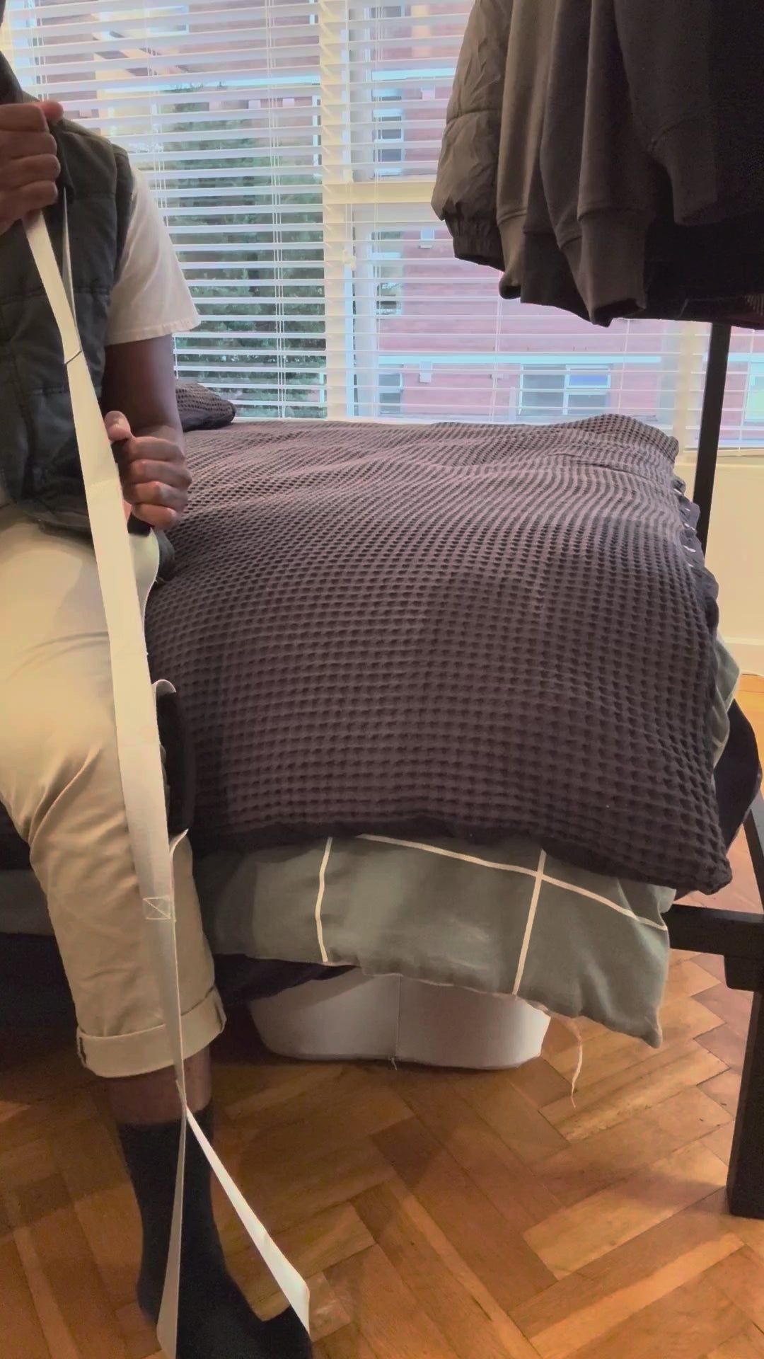 Sitting on the edge of the bed, the foot loop around the heel, using the Triple Grip Leg Lifter to guide the leg up onto the bed